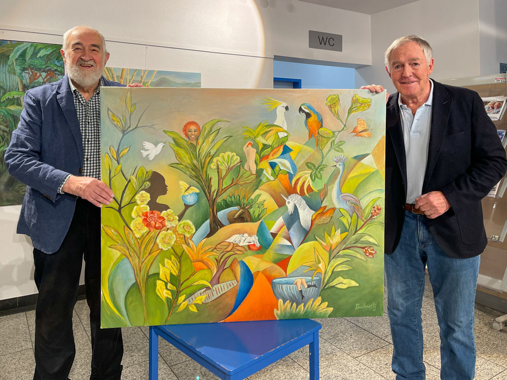 Zwei lächelnde Männer halten ein farbenfrohes Gemälde mit Vögeln, Pflanzen und Blumen.