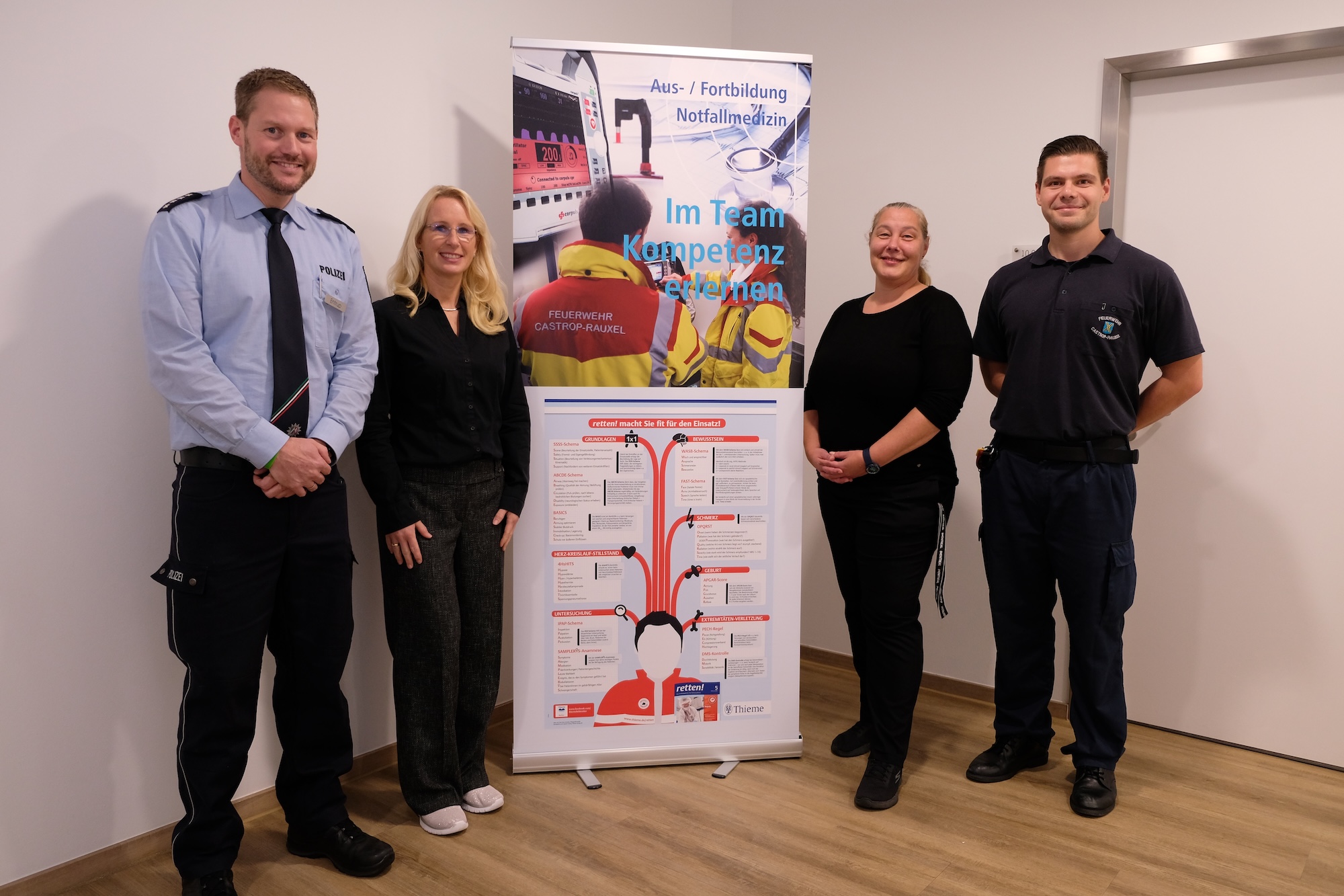 Zwei Männer und zwei Frauen stehen neben einem Roll-up. Die Männer tragen Dienstkleidung der Feuerwehr und der Polizei. 