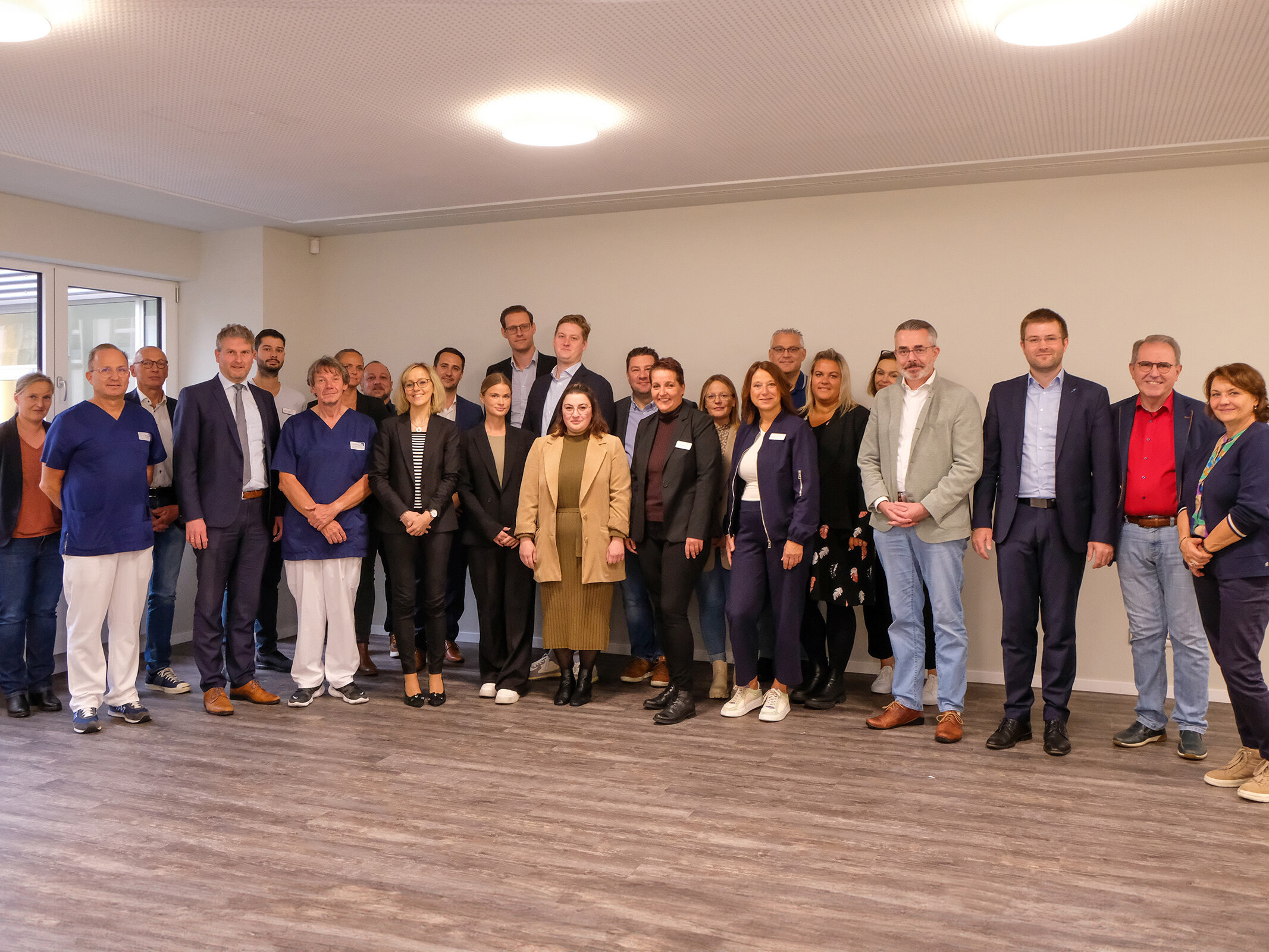 Eine Gruppe von Personen in Geschäftskleidung steht zusammen in einem Raum und posiert lächelnd für ein Gruppenfoto.