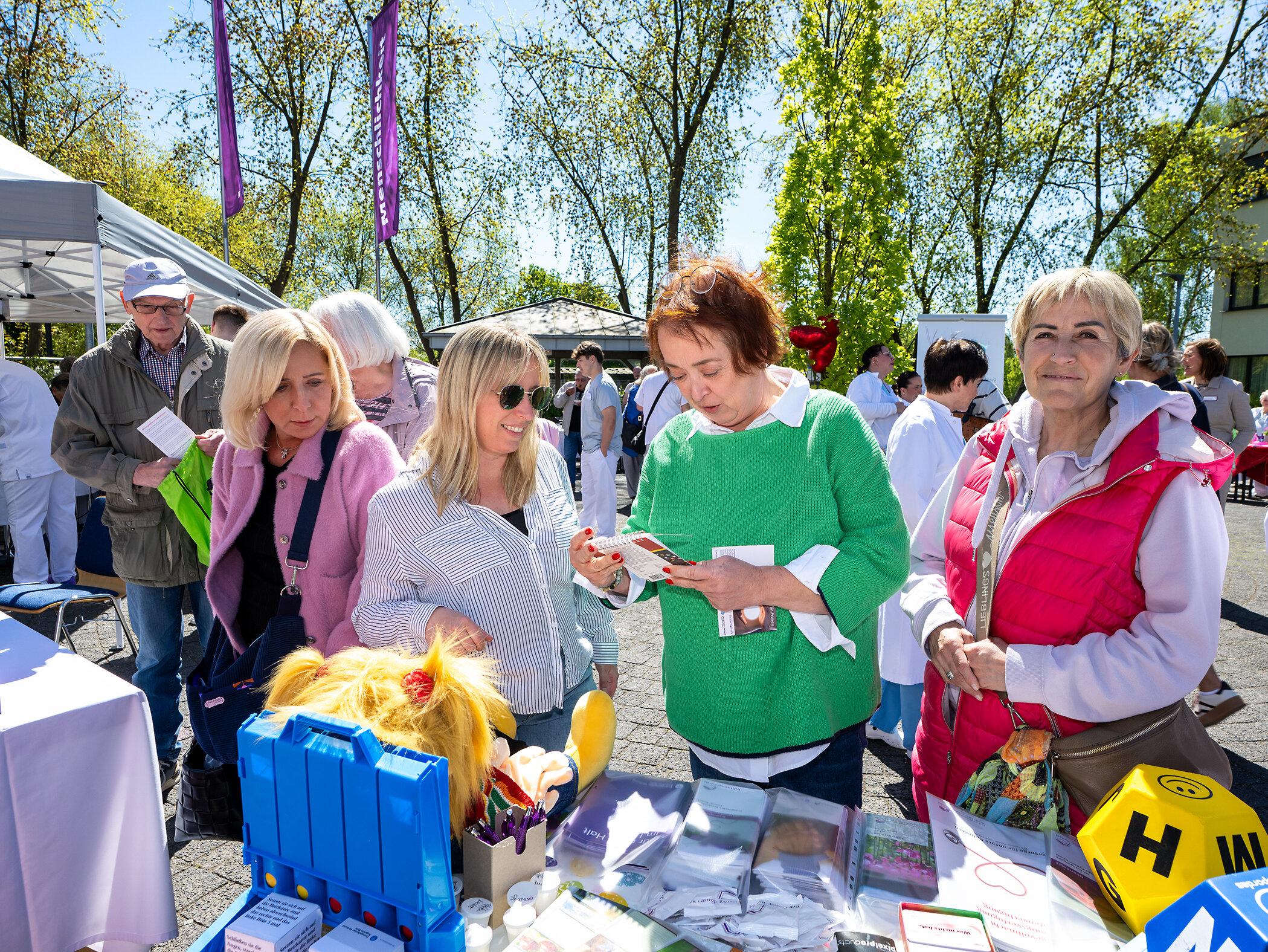 Menschen stehen vor einem Tisch mit Infomaterial. Sie sind draußen und es scheint die Sonne.